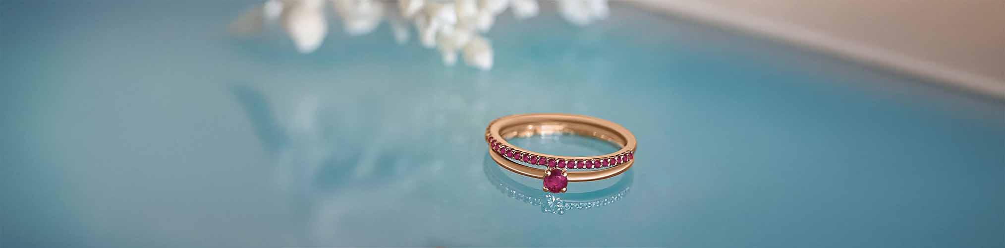 Bague de fiançailles or rose sertie rubis avec pavé de pierres précieuses rouges sur fond bleu aquatique