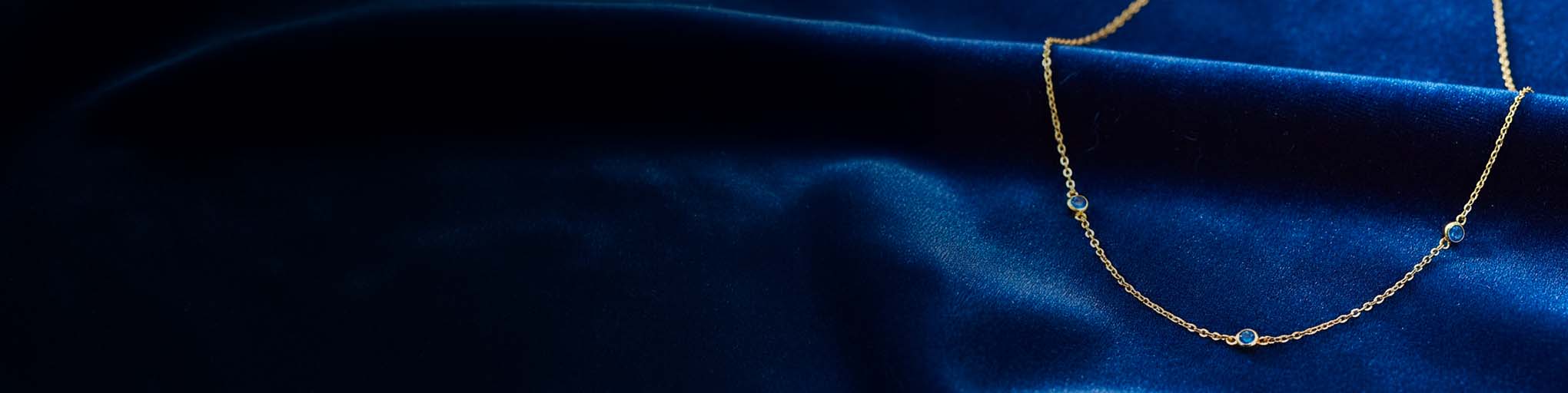 Collier vermeil saphirs bleus sur chaîne fine dorée posé sur soie bleue marine luxueuse joaillerie française