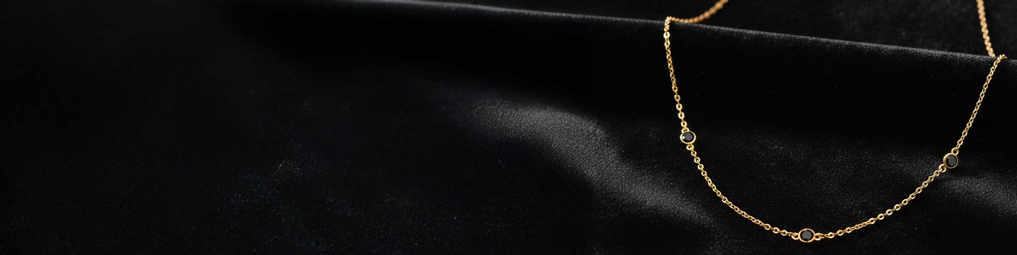 Colliers diamants noirs en vermeil doré sur fond de tissu noir luxueux, joaillerie fine et élégante