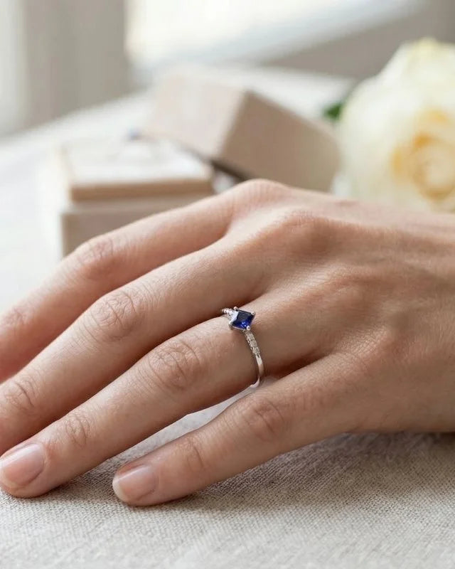 Bague en or blanc 18 carats sertie d'un saphir bleu taille princesse et diamants, portée à l'annulaire