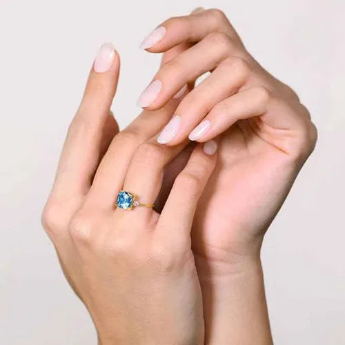 Bague topaze bleue taille coussin en or jaune portée sur les mains
