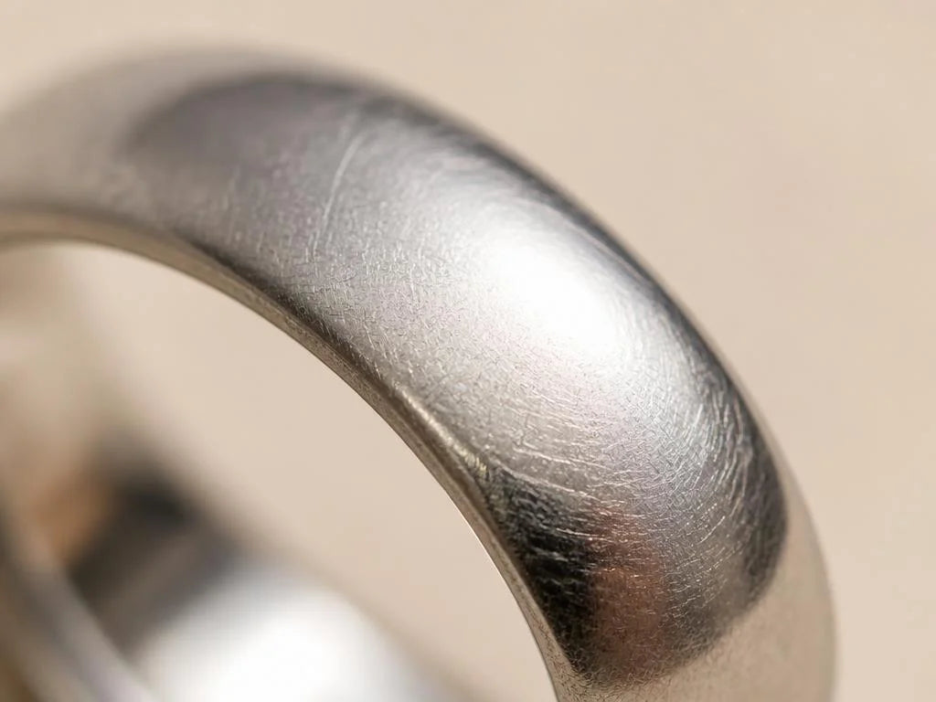 Macro sur la patine satinée d'une alliance en platine portée au quotidien, fines rayures entrecroisées