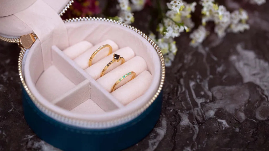 Boîte à bijoux ronde avec compartiments séparés contenant trois bagues en or jaune, rubis et émeraude