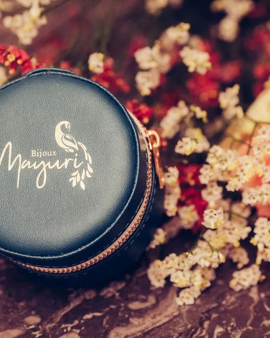 Écrin rond Mayuri en velours turquoise avec bijoux précieux posés sur fond lifestyle fleuri
