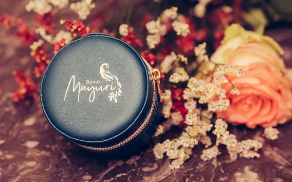Écrin rond Mayuri en velours turquoise avec bijoux précieux posés sur fond lifestyle fleuri