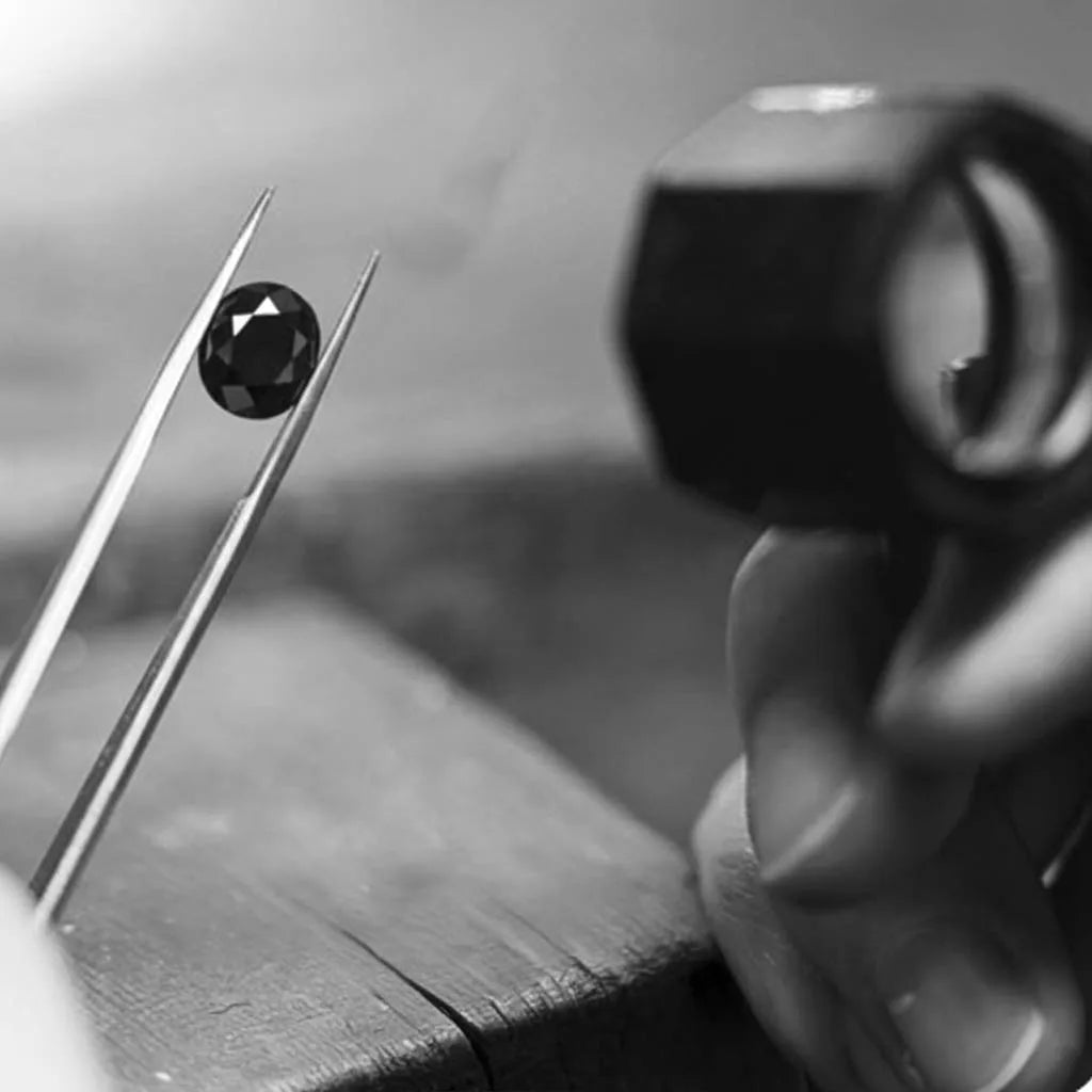 Diamant noir taillé tenu par une pince de gemmologue avec loupe d'inspection en arrière-plan